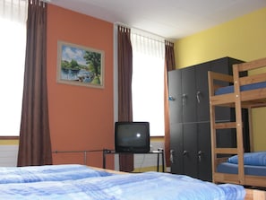 Ein Zimmer mit einem Etagenbett, einem Fernseher auf einem kleinen Tisch, einem Kleiderschrank und einem Bild an der Wand.