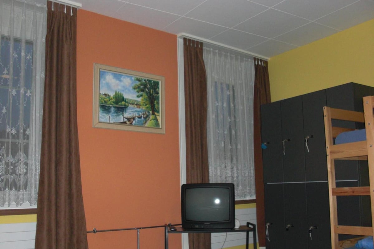 Ein Zimmer mit einem Etagenbett, einem Fernseher auf einem Schrank, einem Bild an der Wand und einem Kleiderschrank.
