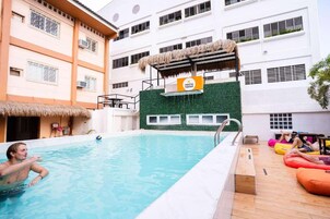 Una piscina interior con estructura de techo de paja, una pared verde con ventanas y un letrero que dice 'nacho hostel'.