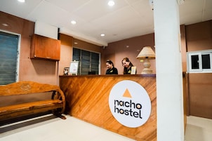 Una recepción con un banco de madera, un reloj y un cartel que dice 'nacho hostel'.