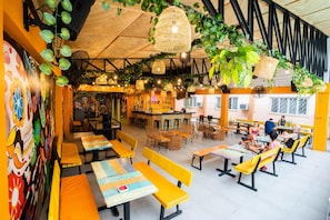 A restaurant with yellow benches and tables, a bar area, and hanging plants. - Nacho Hostel Cebu (Talisay)