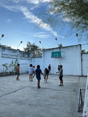 An outdoor basketball court with a basketball hoop, surrounded by a concrete wall and potted plants. - Nacho Hostel Cebu (Talisay)