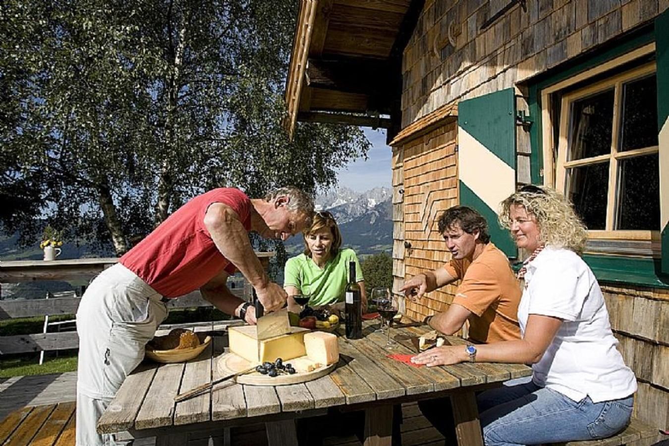 A wooden cabin with a dining table set outdoors, surrounded by trees and a mountain view.