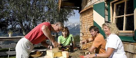A wooden cabin with a dining table set outdoors, surrounded by trees and a mountain view.