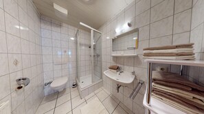 Ein modernes Badezimmer mit einer gläsernen Duschkabine, Toilette, Waschbecken und Handtuchhalter.