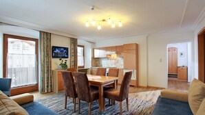 A modern living room with a dining area, a kitchen, and a TV mounted on the wall. - Appartements Kalswirt (Kirchberg in Tirol)