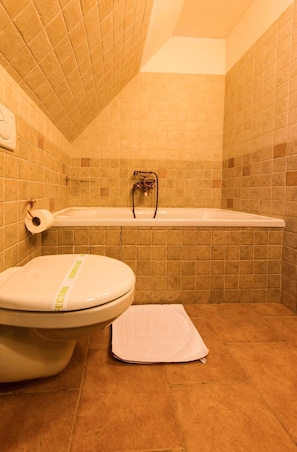 A bathroom with a bathtub, toilet, and a towel on the floor. - Hotelliptovský Dvor (Liptovský Ján)