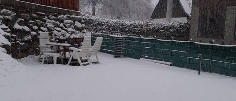Un espacio exterior cubierto de nieve con una mesa y sillas, un muro de piedra y una valla de madera.
