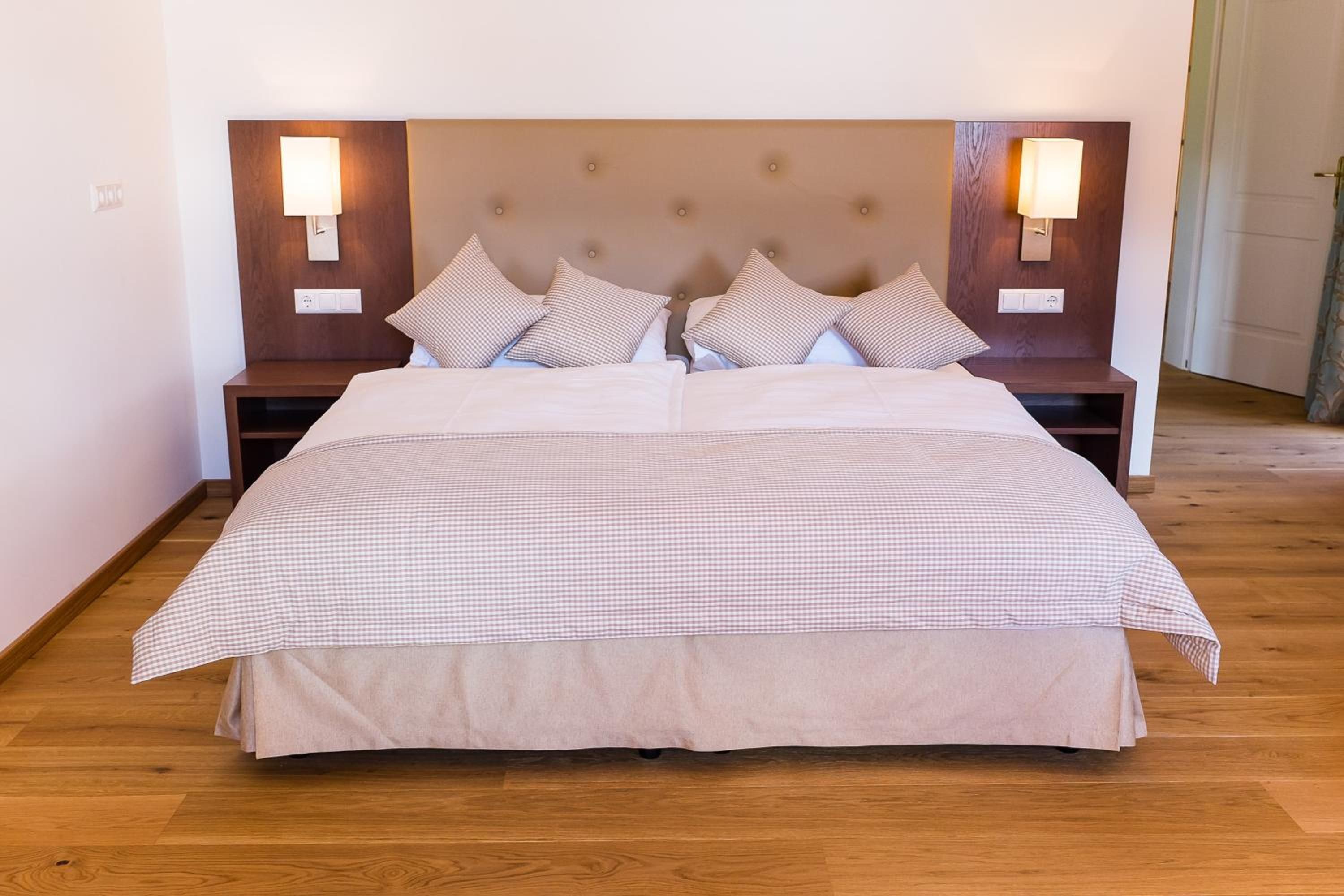 Ein Doppelbett mit kariertem Überwurf, zwei Nachttische mit Lampen und ein Holz-Kopfstück.