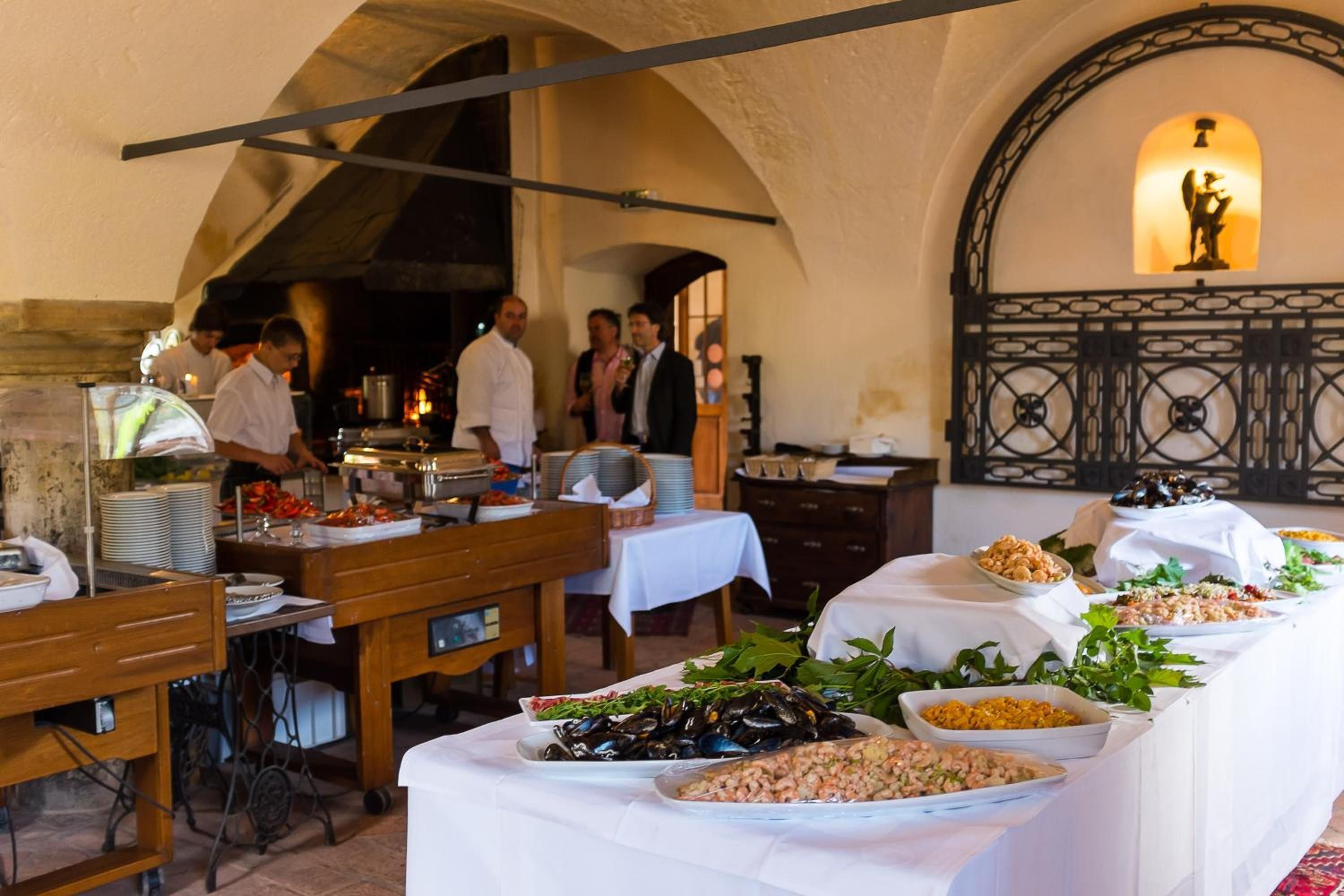 Ein reichhaltiges Buffet mit verschiedenen Speisen und eine Gruppe von Personen in einem Essbereich mit einer Rundbogenzelle.