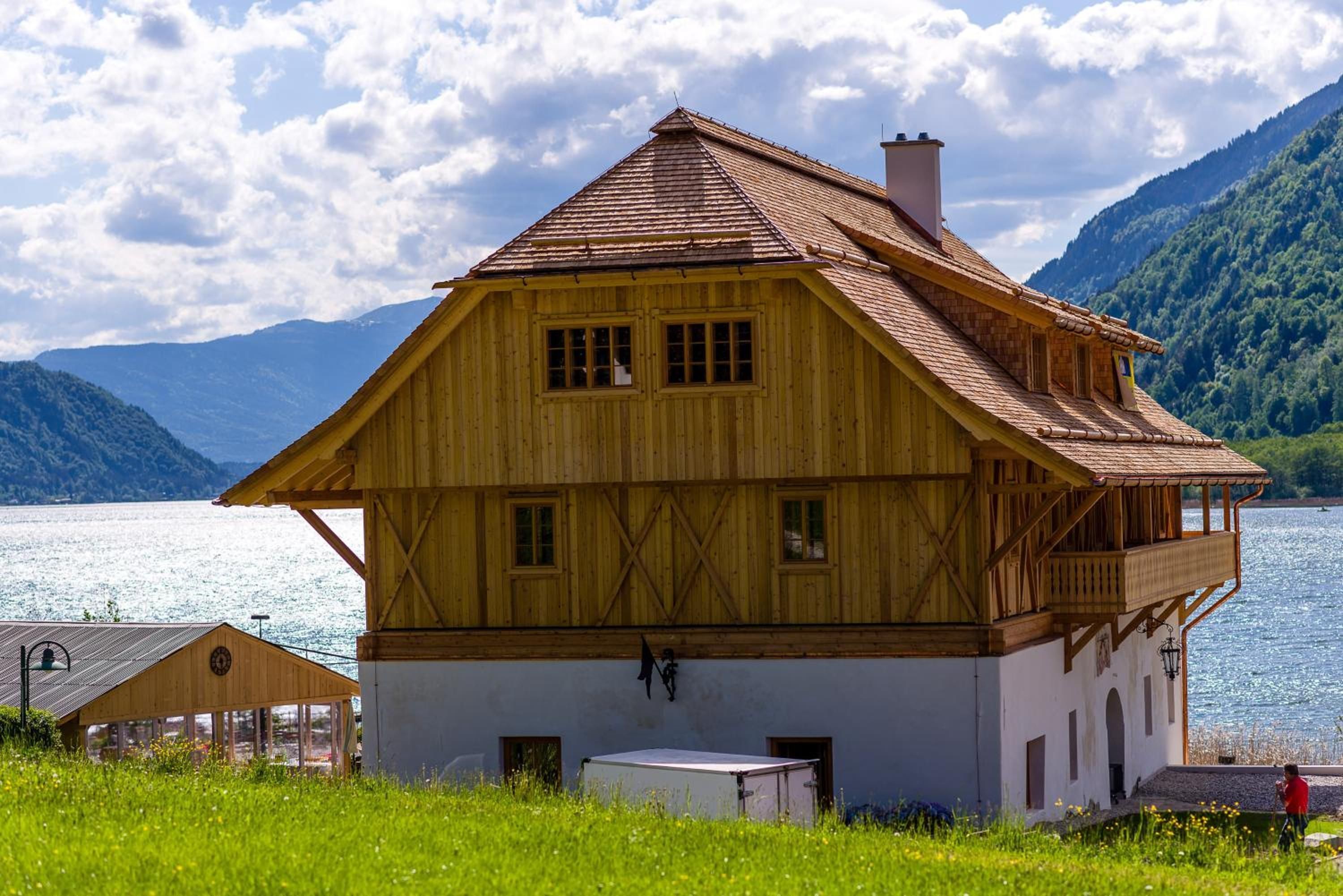 Eine Holzhütte mit Balkon, einem kleinen Anbau und Blick auf einen See und Berge.