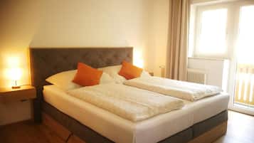 Ein Doppelbett mit Kopfteil, zwei Kissen, ein Nachttisch mit Lampe und ein Fenster mit Vorhängen.