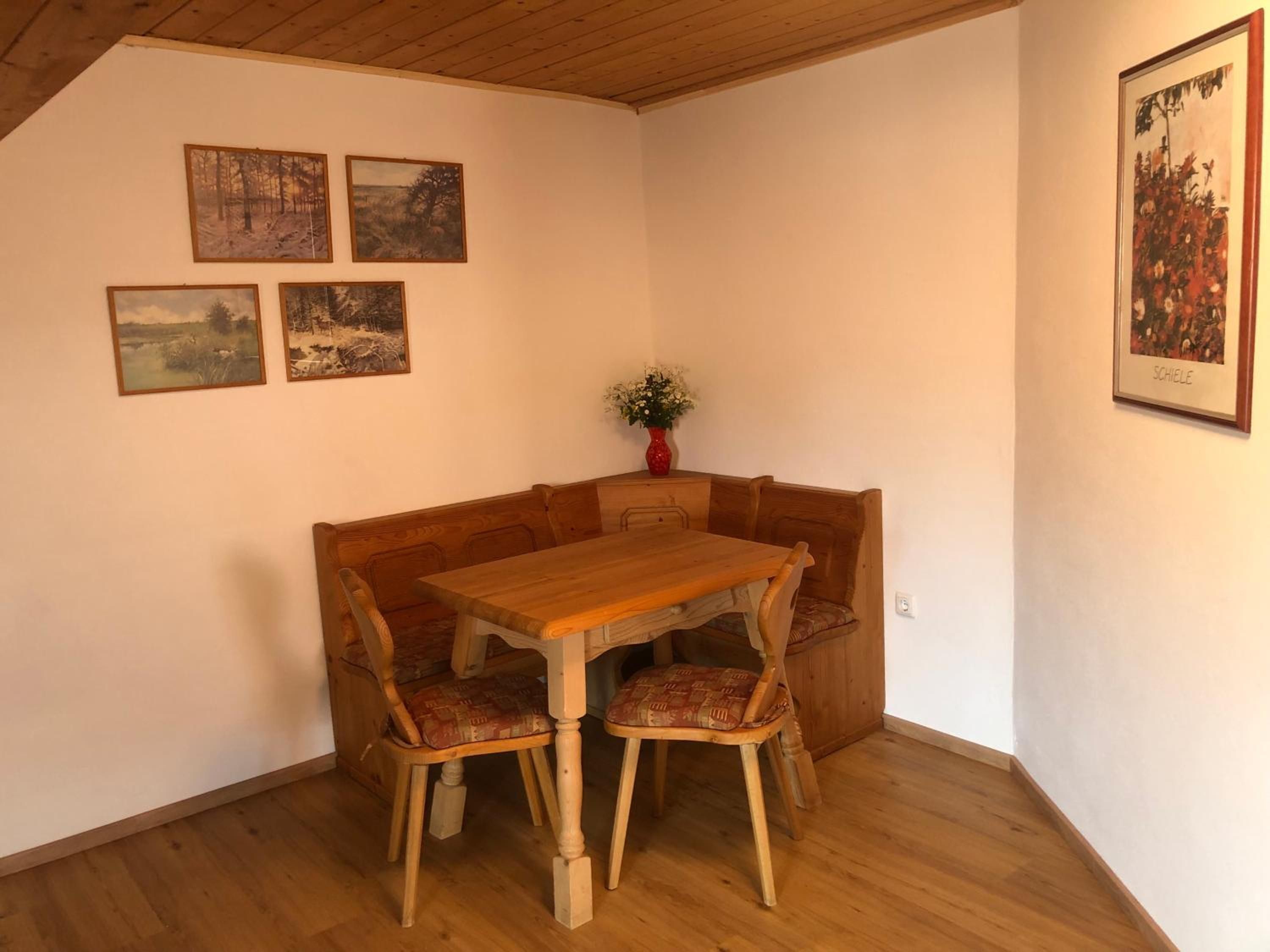 A corner dining area with a wooden table and bench, surrounded by four framed landscape paintings.