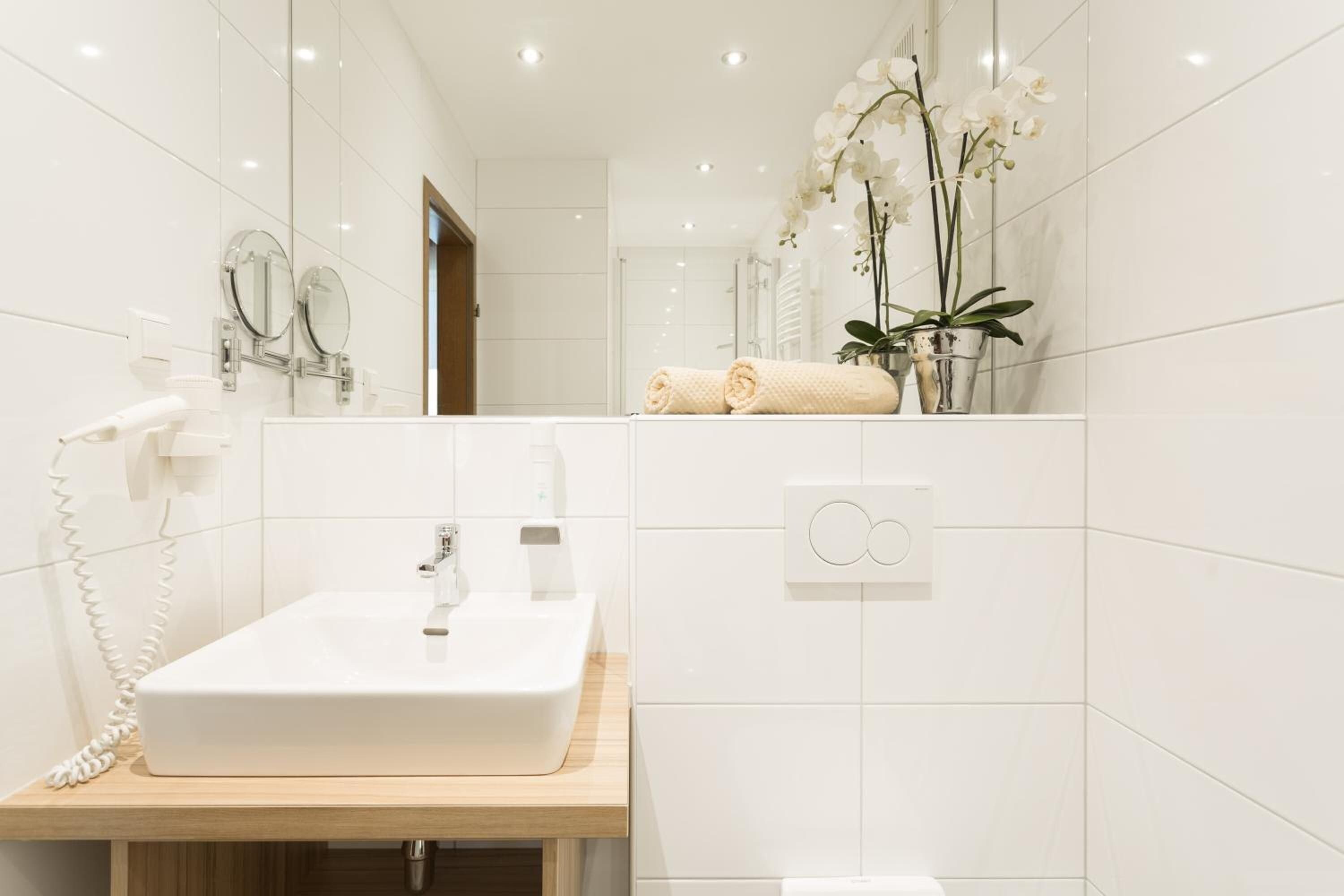 Ein Badezimmer mit einem weißen Waschbecken, einem Spiegel, einem Handtuch und einer Orchidee im Topf.