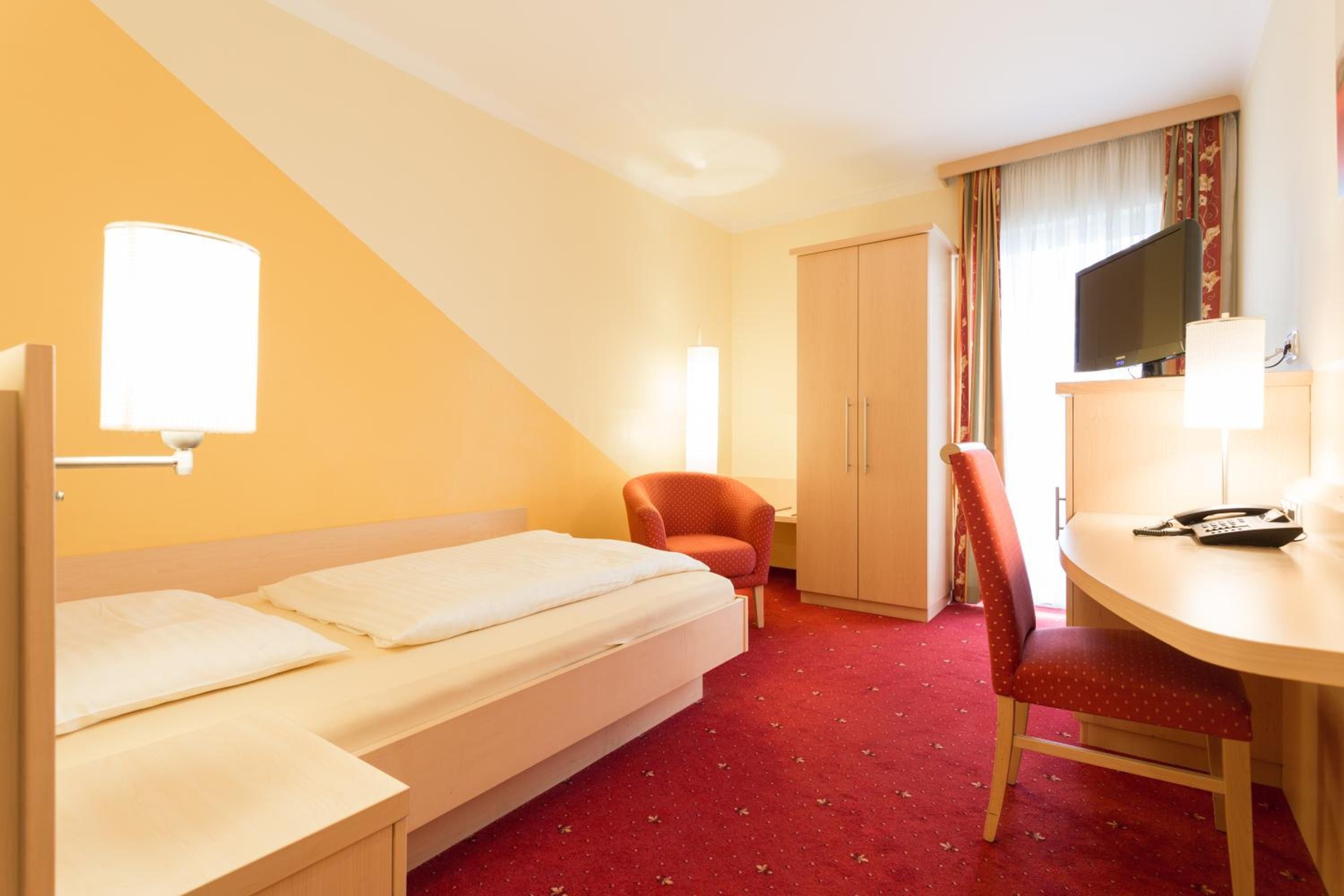 Ein Hotelzimmer mit Bett, Schreibtisch, Stuhl, Kleiderschrank und Fernseher.