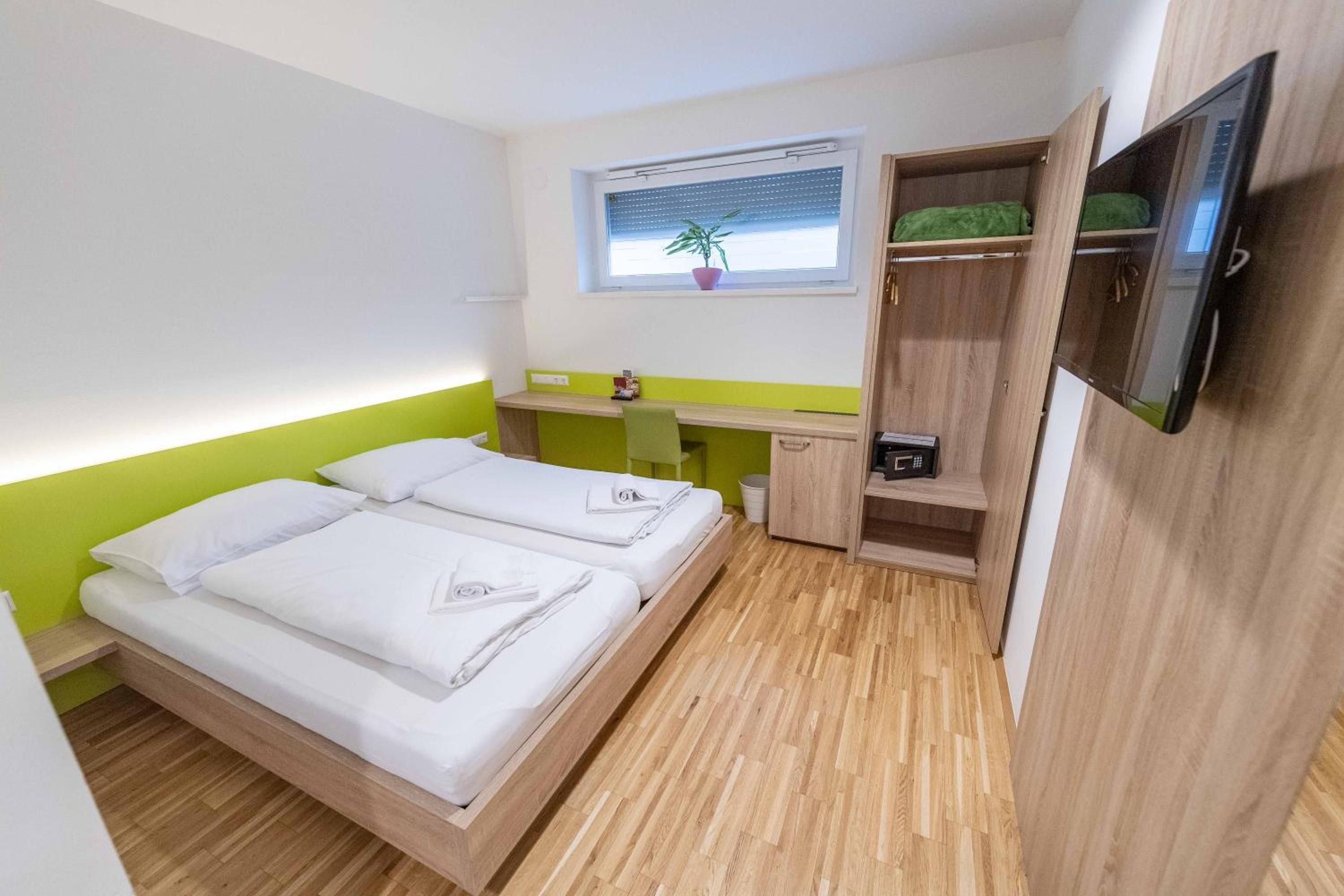 Habitación de hotel pequeña con dos camas, un escritorio, un televisor y una ventana con una planta.