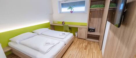 Habitación de hotel pequeña con dos camas, un escritorio, un televisor y una ventana con una planta.