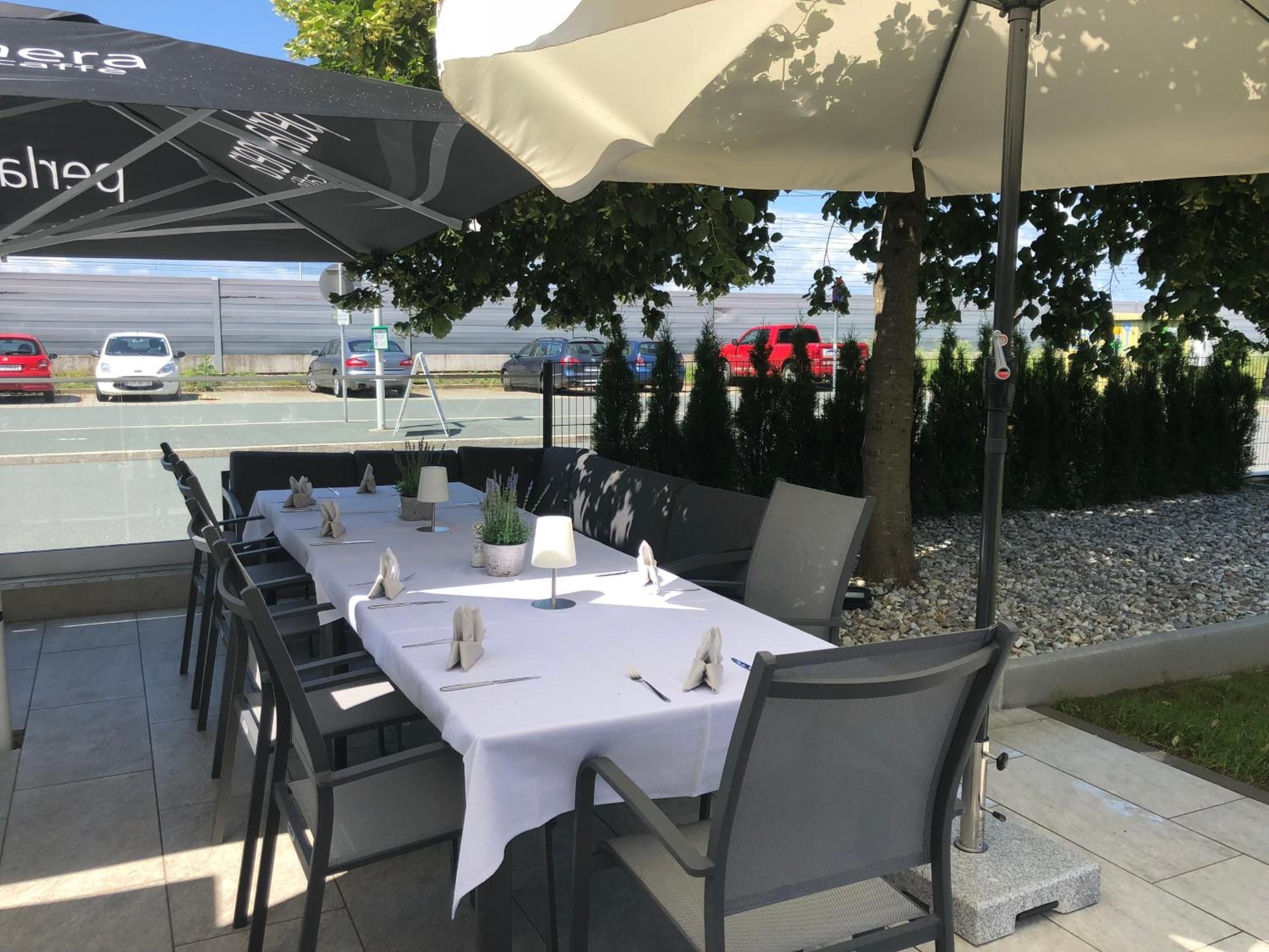 Un espace de restauration en plein air avec des tables pour deux, protégées par des parasols, et des chaises disposées autour.