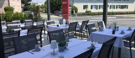 An outdoor dining area with tables set for two, chairs, and potted plants.