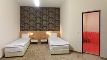 A hotel room with two single beds, a patterned headboard, a red door, and a carpeted floor.
