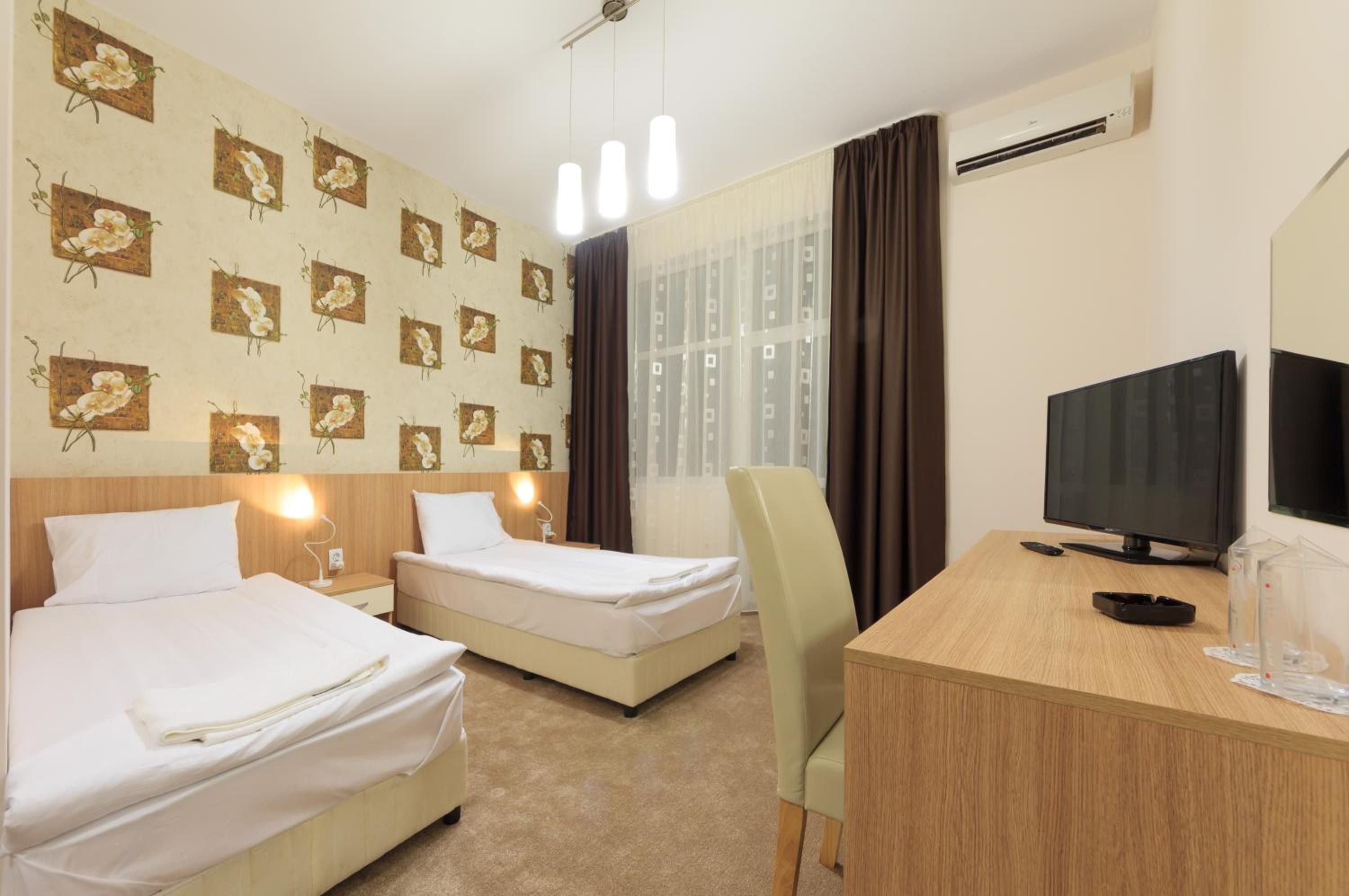 Habitación de hotel con dos camas, un escritorio con televisor y una ventana con cortinas.