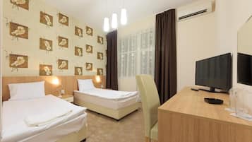 Habitación de hotel con dos camas, un escritorio con televisor y una ventana con cortinas.