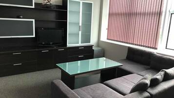 A modern living room with a glass coffee table, grey sofa, dark cabinets, and a television.