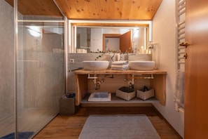 A modern bathroom with a wooden ceiling, two sinks, a glass shower enclosure, and a mirror above the sinks. - Wellnesshaus Reichelt (Radstadt)