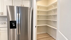 Ein Edelstahl-Kühlschrank von Whirlpool mit Wasserspender, weißen Schränken und einem eingebauten Vorratsschrank mit mehreren Regalen.