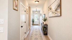 A hallway with a patterned rug, a console table with a plant, and a door at the end. - Tiger Country Retreat in Baton Rouge - CB1008 (Baton Rouge)
