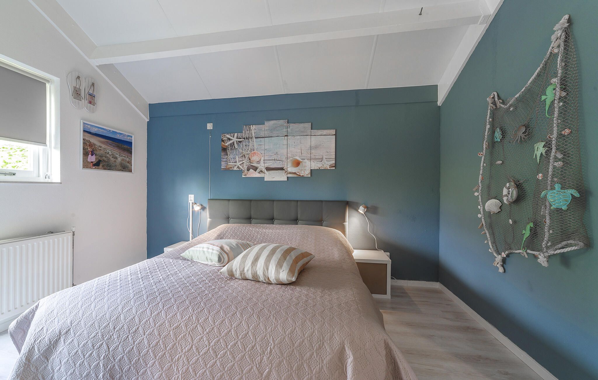 A bedroom with a bed, a wall-mounted artwork, and a decorative net with sea creatures.