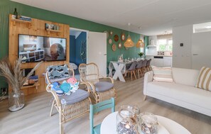 Ein Wohnzimmer mit Fernseher, Korbstühlen, einem weißen Sofa und einem Essbereich mit Tisch für vier Personen.