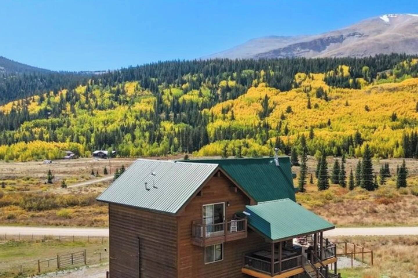 Een houten chalet met een groen dak, een balkon en uitzicht op een bebost berglandschap.