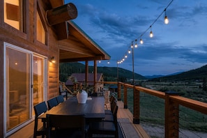A wooden deck with a table and chairs, overlooking a mountainous landscape.