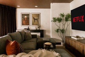 A modern living room with a sectional sofa, a coffee table, a TV mounted on the wall, and a plant.