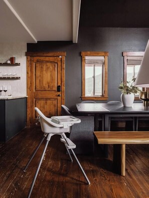 A modern kitchen with a wooden door, a dining table with a bench, and a high chair.