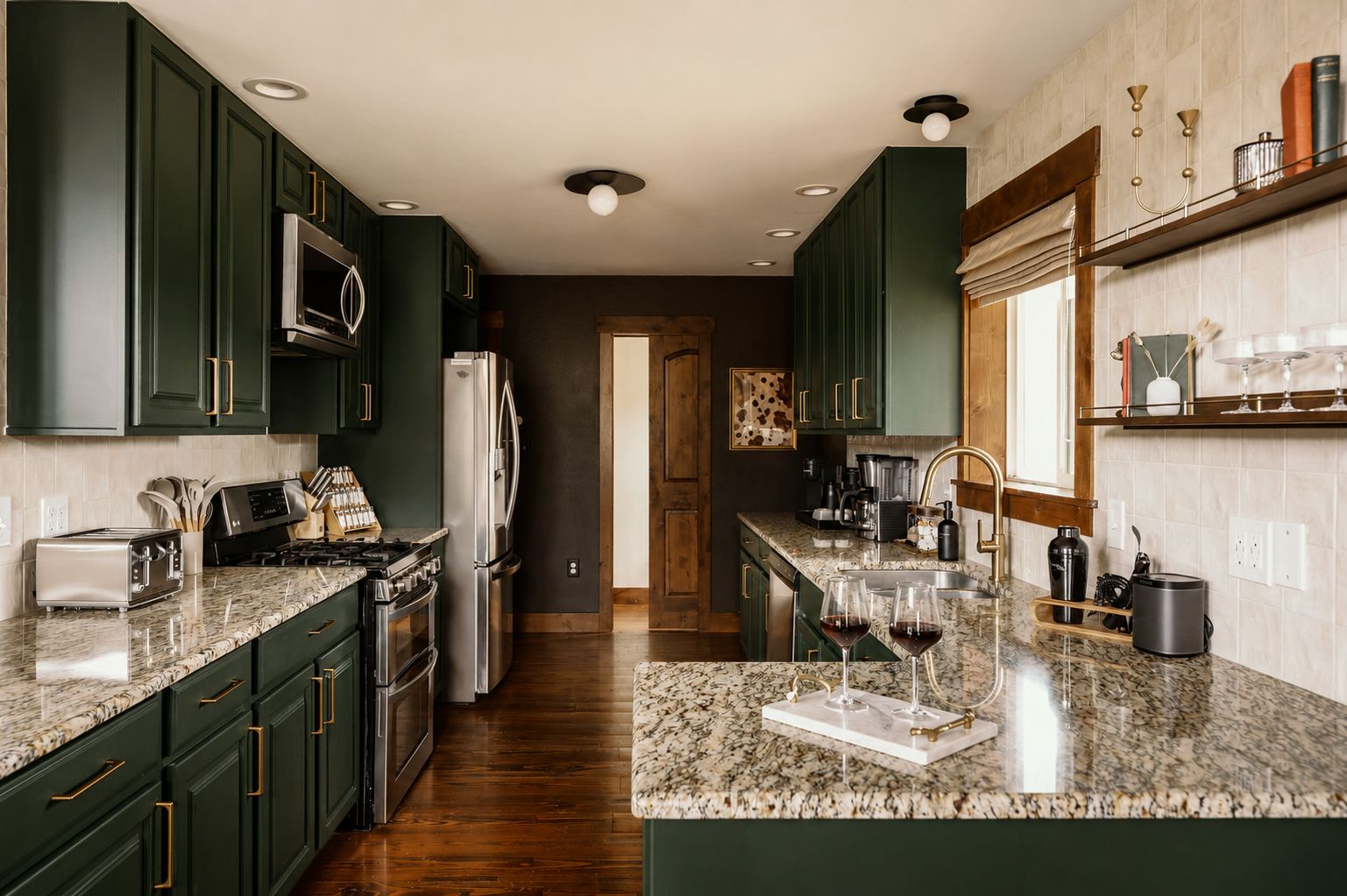 Una cocina con armarios verde oscuro, electrodomésticos de acero inoxidable, encimera de granito y ventana con vistas.