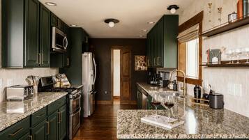 Una cocina con armarios verde oscuro, electrodomésticos de acero inoxidable, encimera de granito y ventana con vistas.