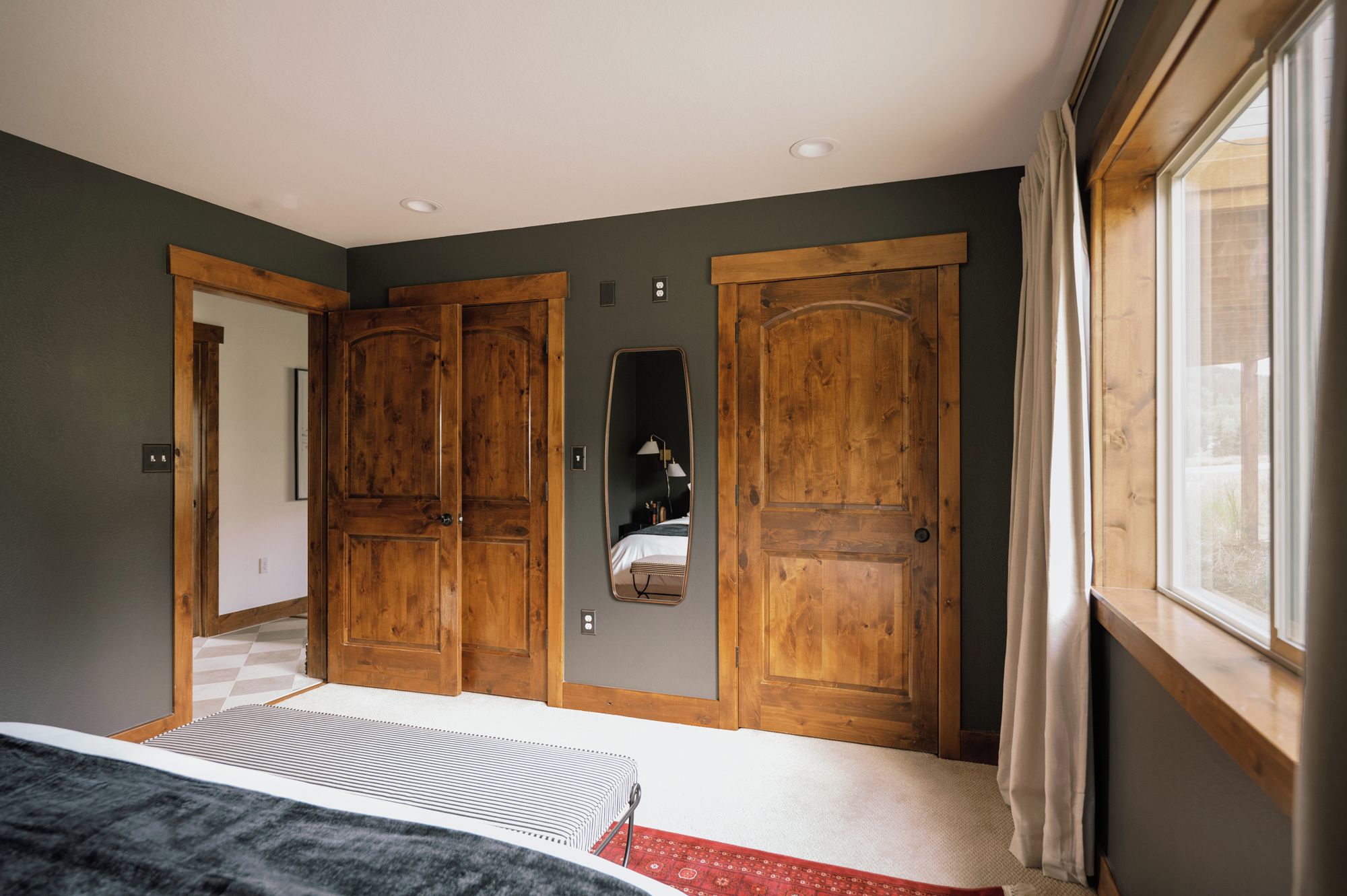 Un dormitorio con dos armarios de madera, una cama con colcha a rayas, un espejo y una ventana con cortinas.