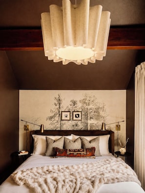 A bedroom with a bed, a wall-mounted lamp, a framed picture, and a ceiling light fixture.
