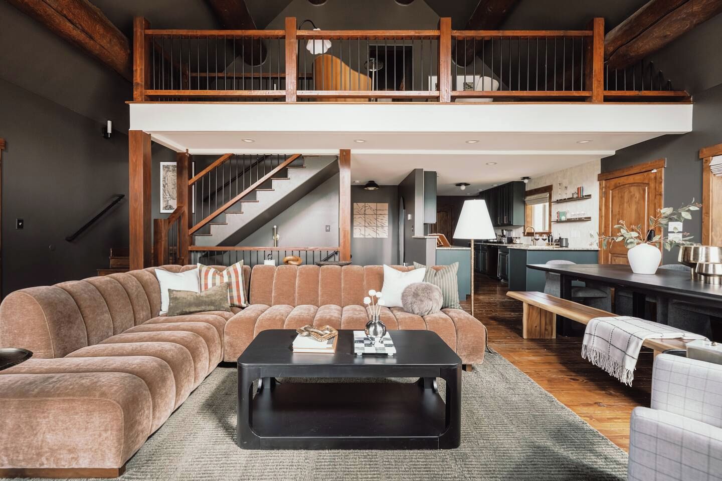 A spacious living area with a large sectional sofa, a black coffee table, and a wooden staircase leading to an upper level.
