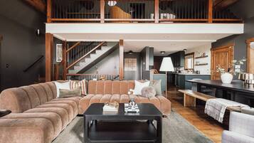 A spacious living area with a large sectional sofa, a black coffee table, and a wooden staircase leading to an upper level.