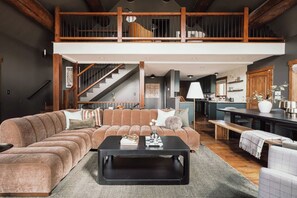 A spacious living area with a large sectional sofa, a black coffee table, and a wooden staircase leading to an upper level.