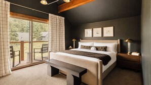 A bedroom with a large bed, a bench, a nightstand, a lamp, and a view of the outdoors. - Epic Views, Sauna, Dog Lovers 5BR, 25 min to Breck (Breckenridge)
