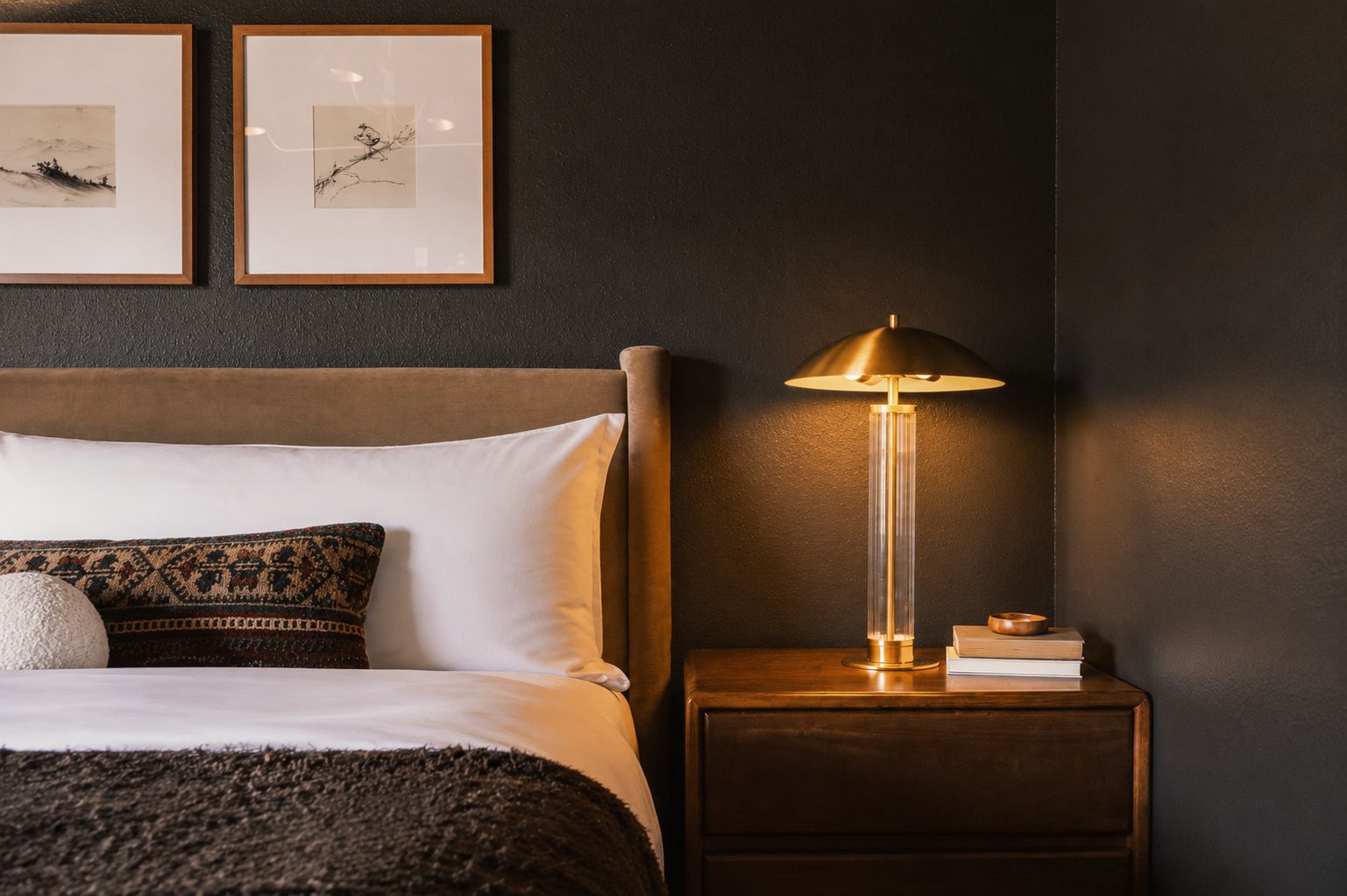 Un lit bien fait, avec une tête de lit, une lampe de chevet et deux œuvres d’art encadrées accrochées au mur.
