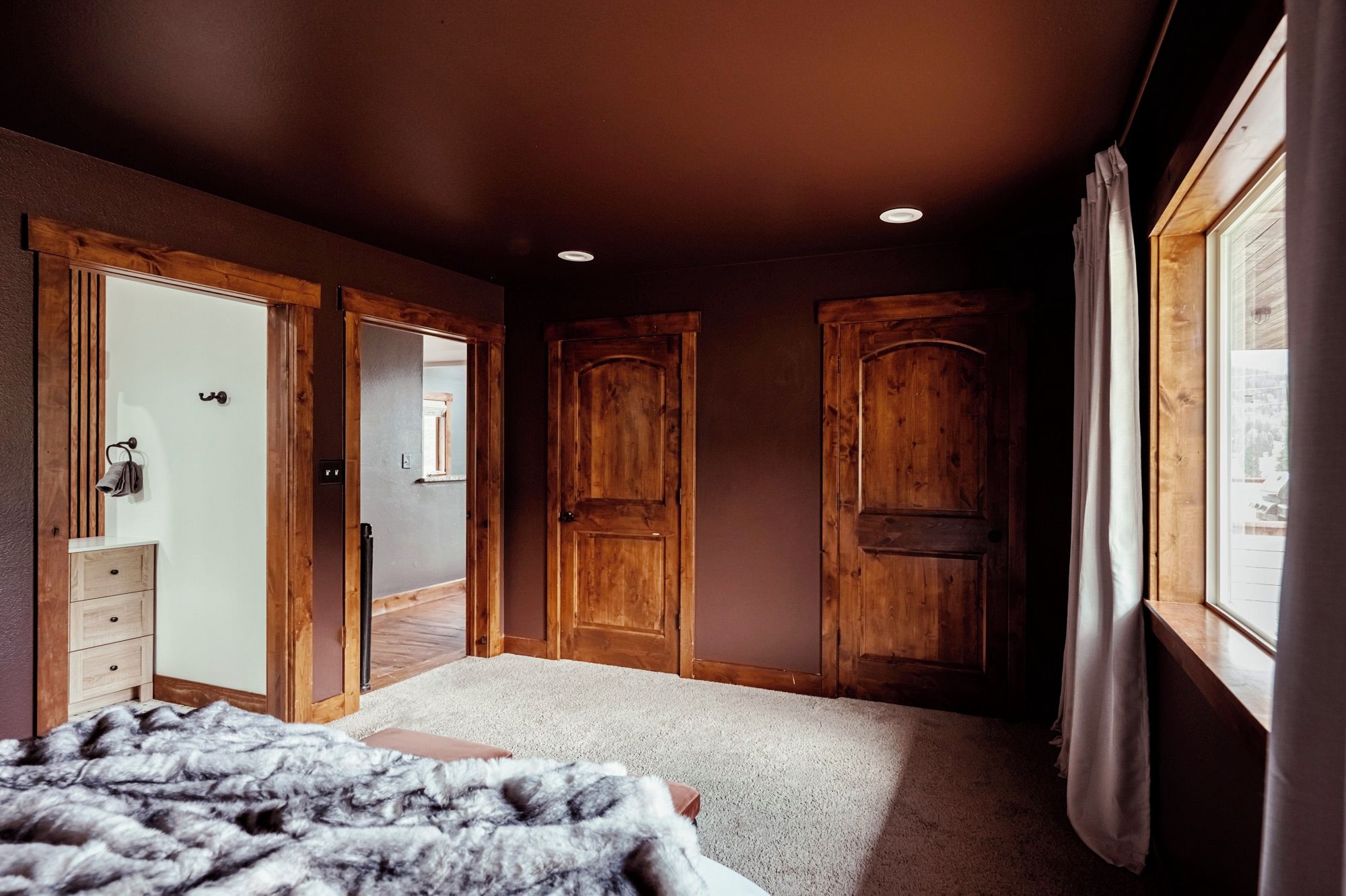 Un dormitorio con cama, cómoda, ventana y puertas de madera.