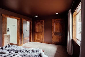 A bedroom with a bed, a dresser, a window, and wooden doors.