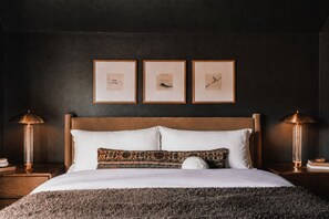 A neatly made bed with a patterned pillow, a headboard, and framed pictures on the wall.