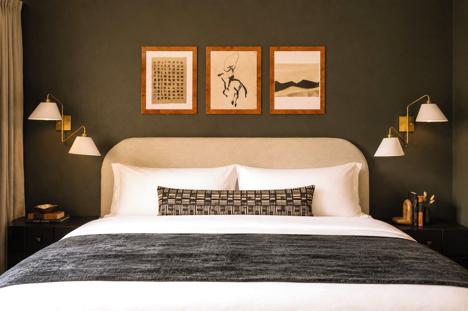 A hotel room with a large bed, two bedside tables, a headboard, and three framed artworks on the wall.