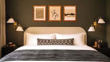 A hotel room with a large bed, two bedside tables, a headboard, and three framed artworks on the wall.